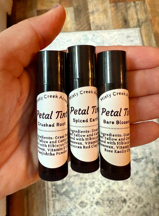 Three small bottles of Misty Creek Naturals held in a hand with a wooden surface in the background.