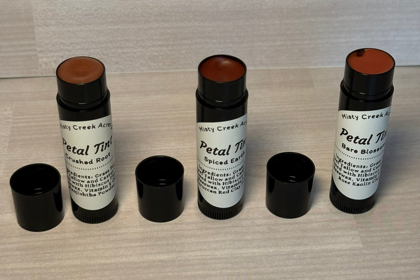 Three cosmetic sticks with black caps on a textured surface