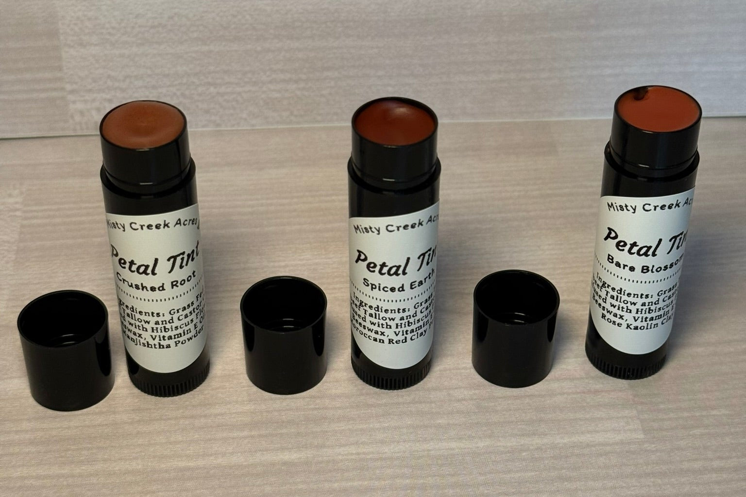 Three cosmetic sticks with black caps on a textured surface