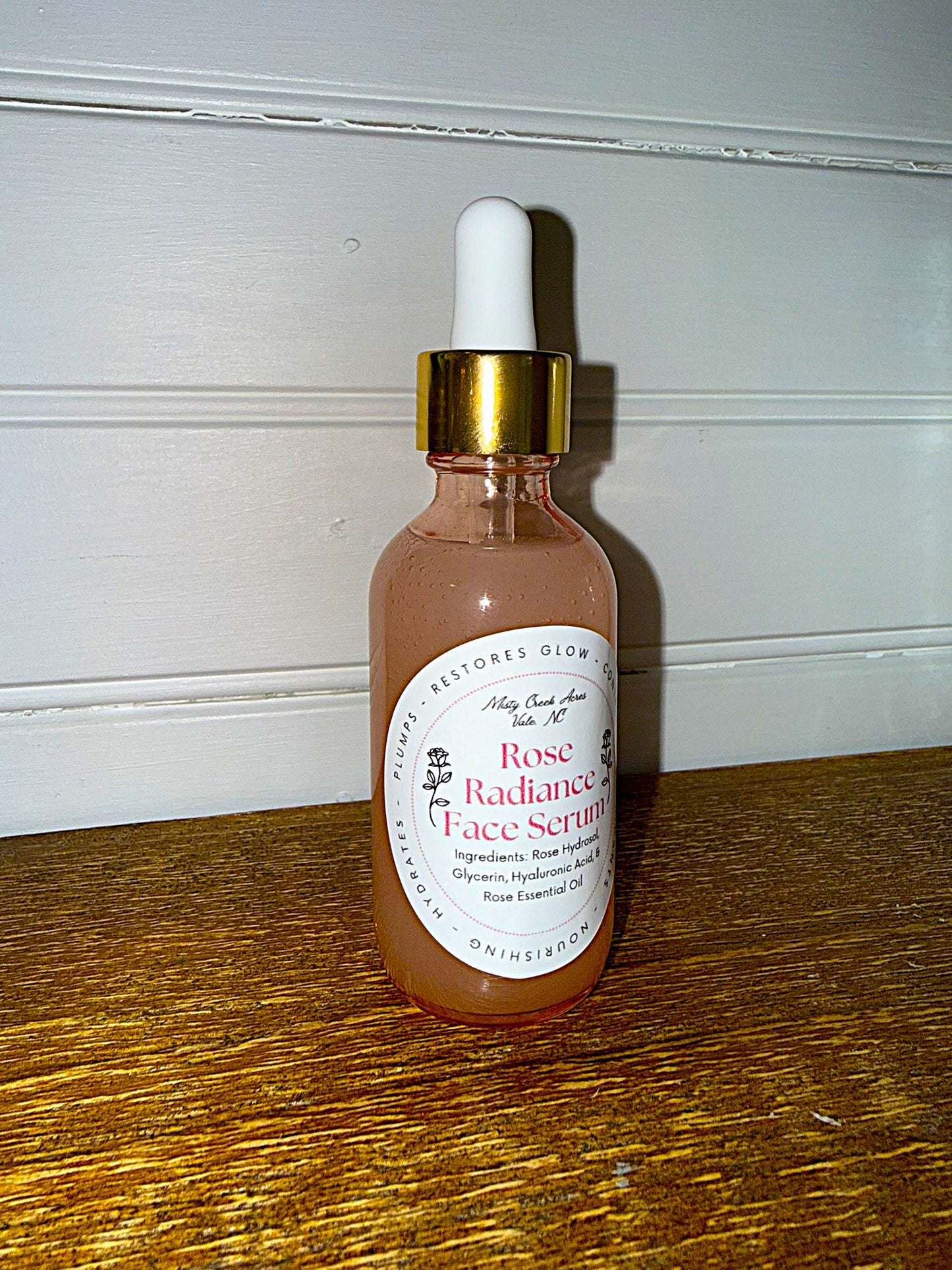 Bottle of Rose Radiance Face Serum with dropper on a wooden surface