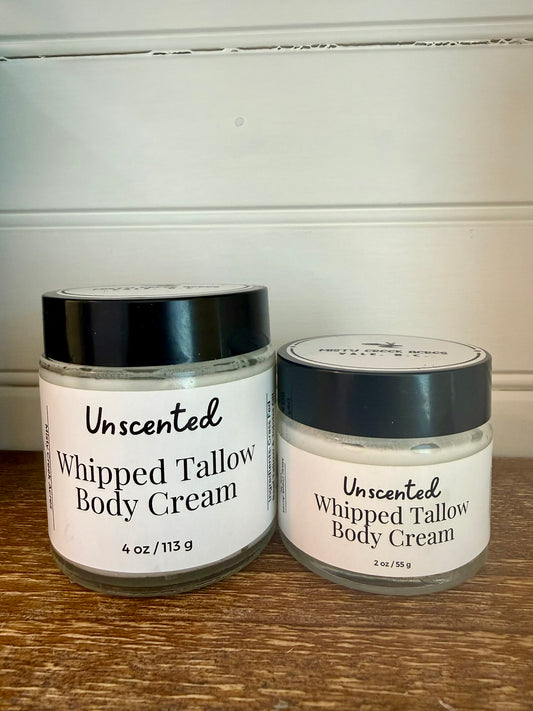 Two jars of unscented whipped tallow body cream on a wooden surface with a white wall background.