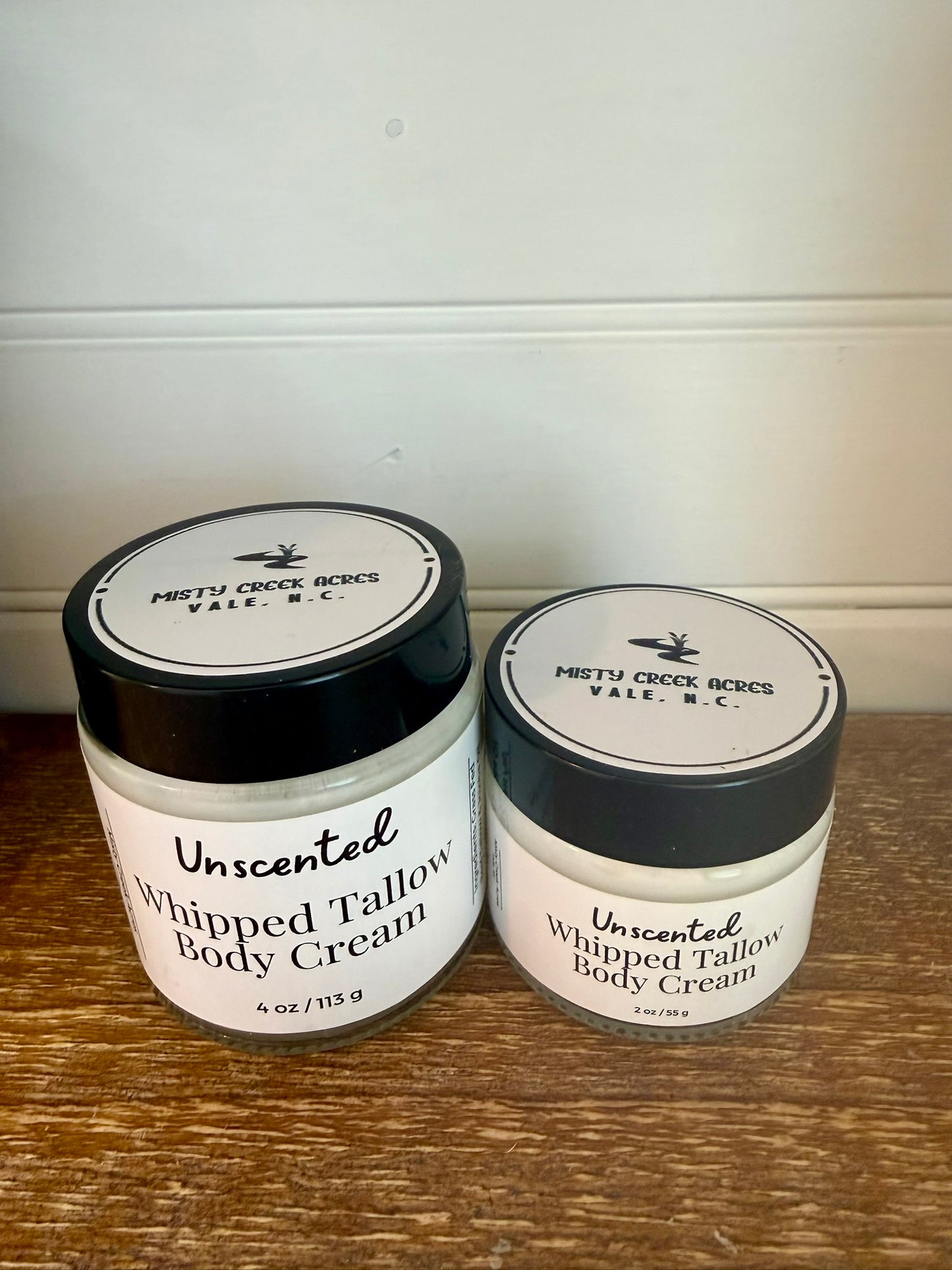 Two jars of Unscented Whipped Tallow Body Cream on a wooden surface with a white background.