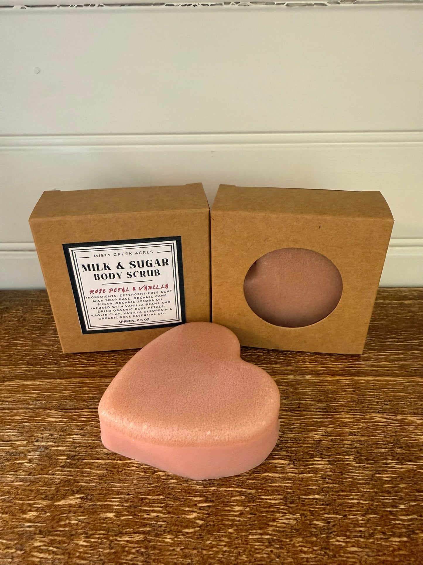 Heart-shaped pink body scrub with a brown box on a wooden surface