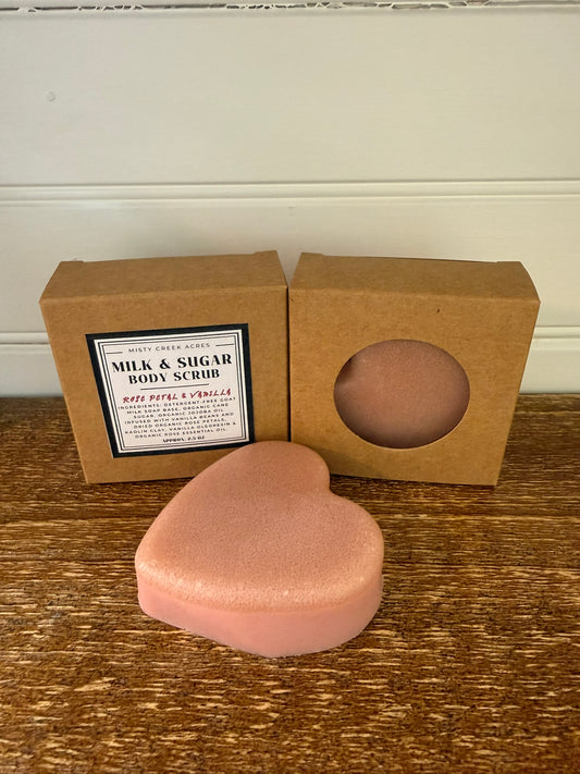 Heart-shaped pink body scrub with a brown box on a wooden surface