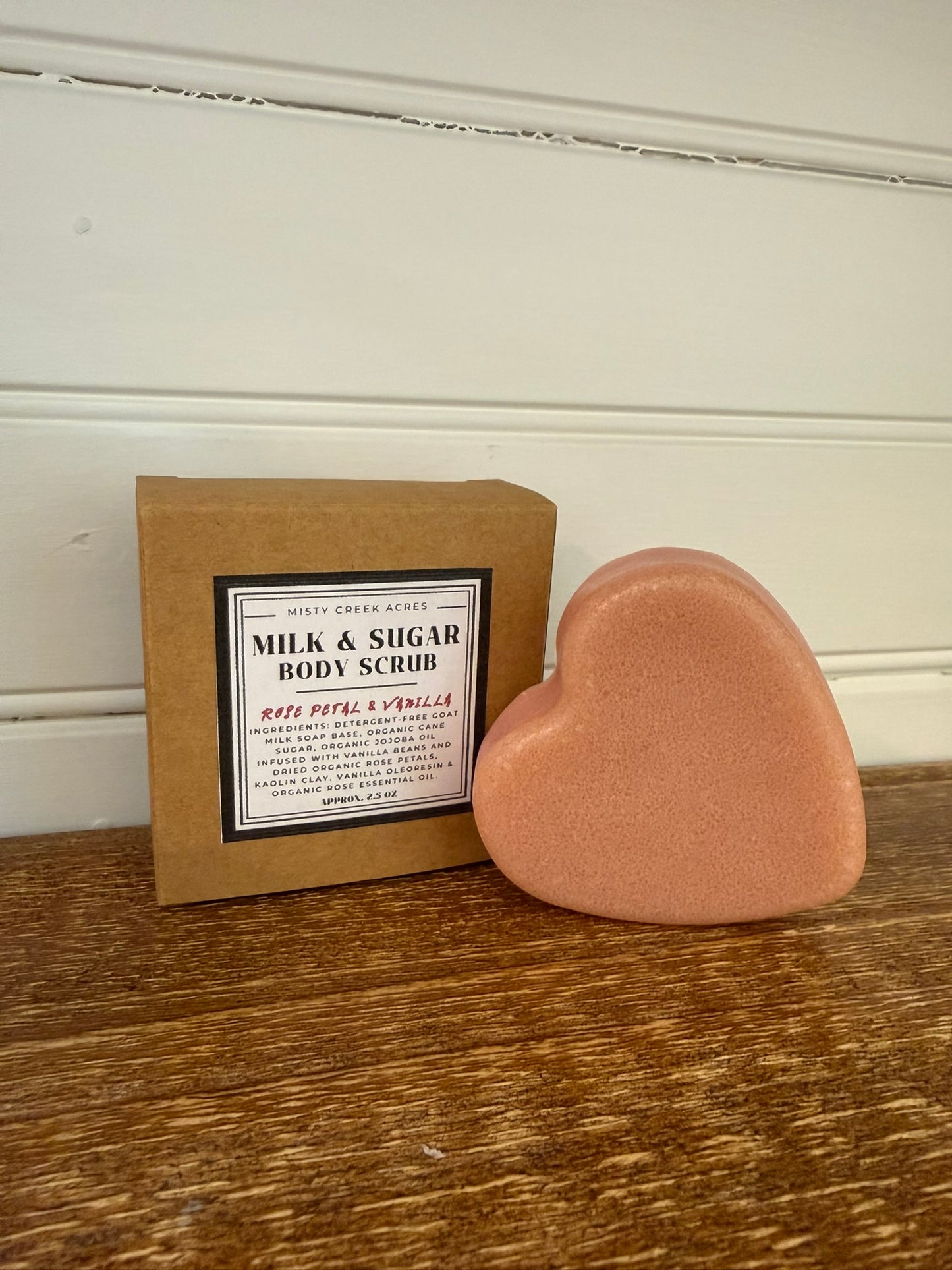 Heart-shaped body scrub and packaging on a wooden surface with a white wall background