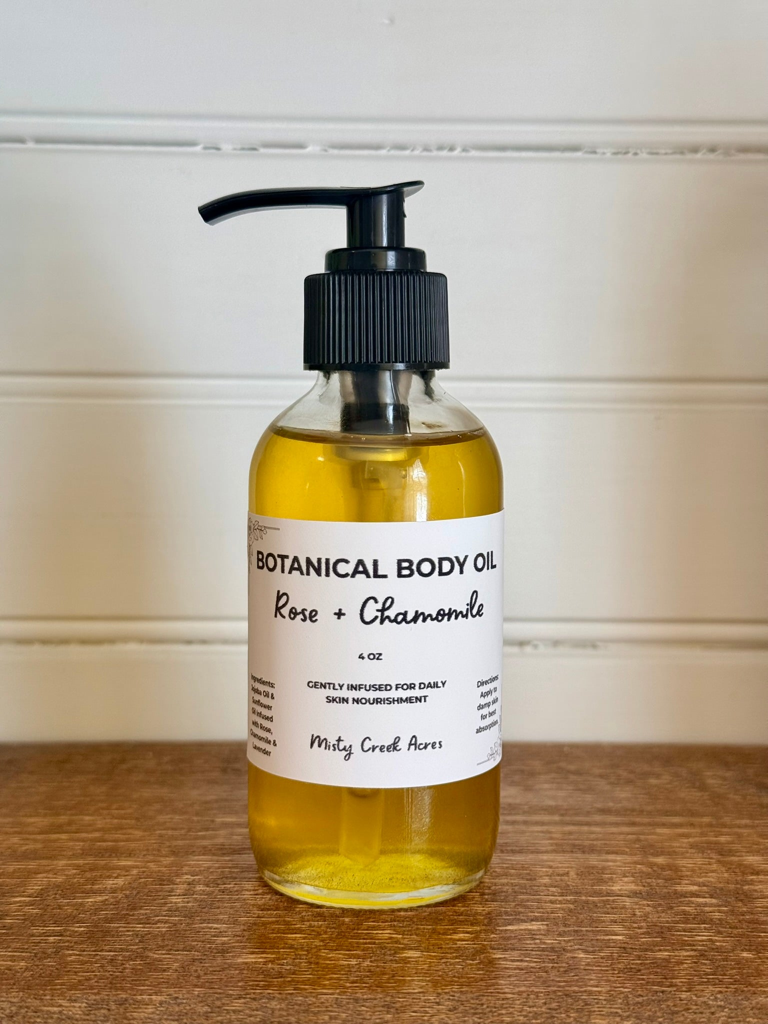 Bottle of botanical body oil with a pump on a wooden surface and white wall background