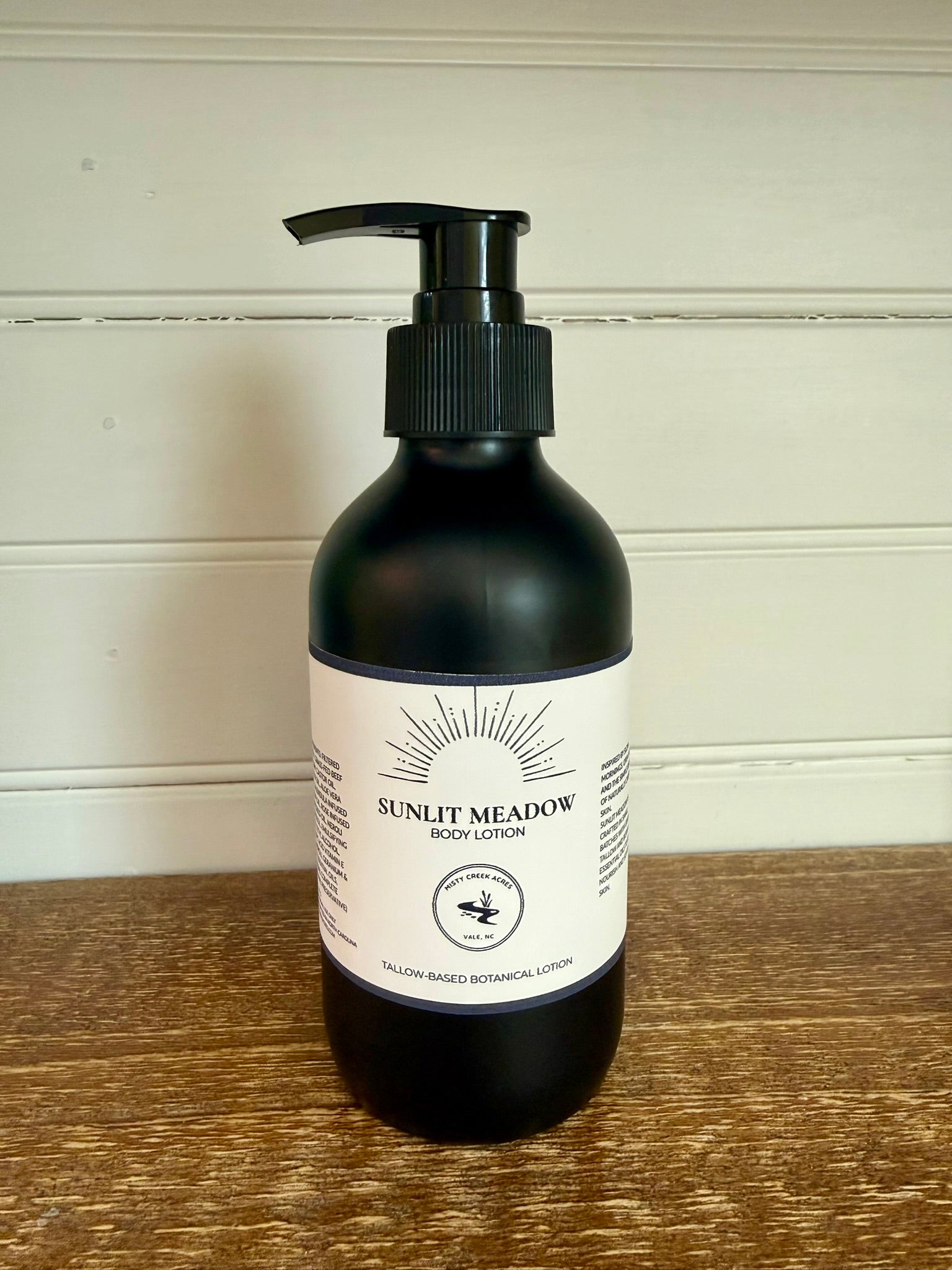 Black lotion bottle with pump on a wooden surface and white wall background