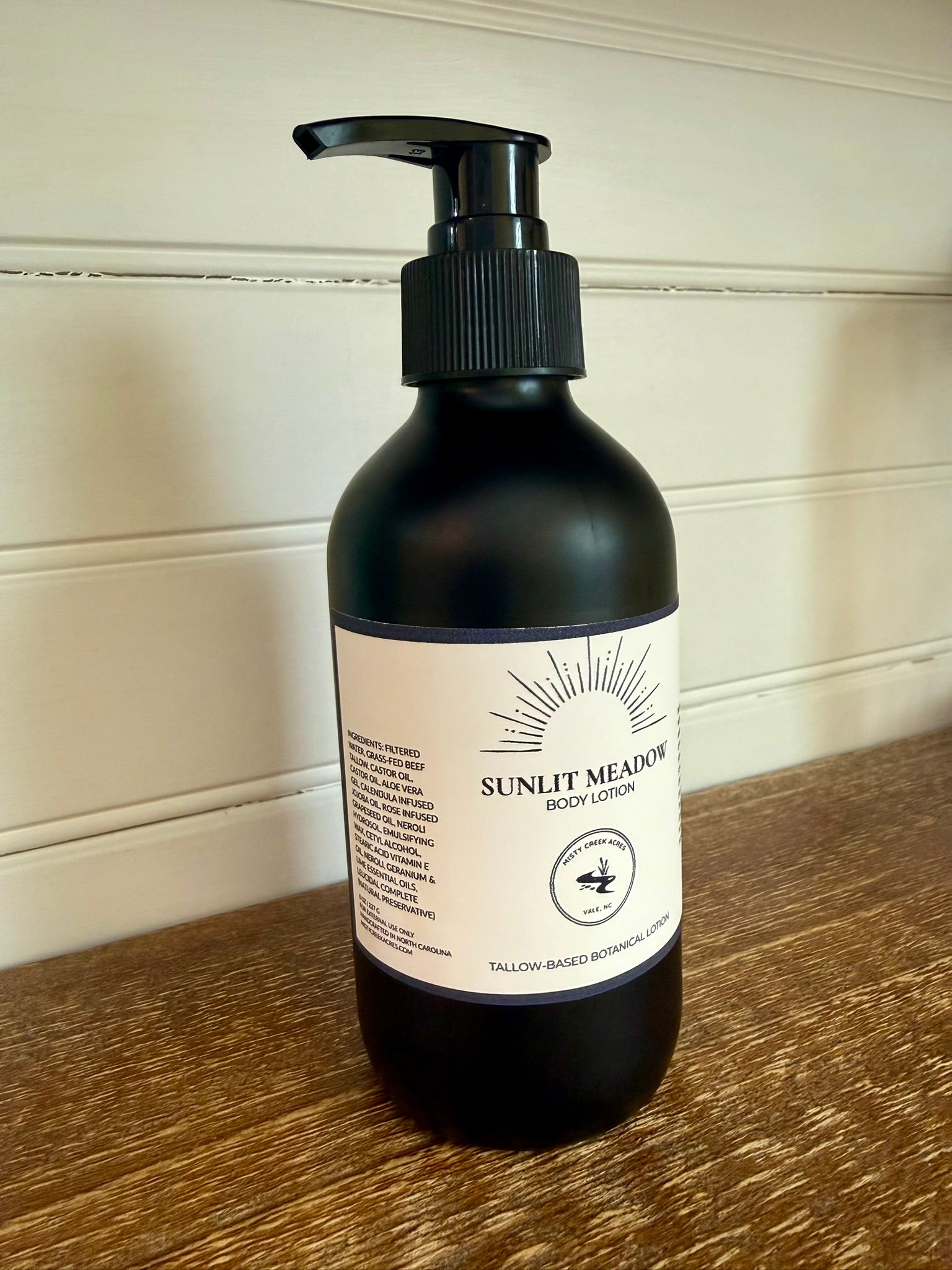 Black bottle of Sunset Meadow body lotion on a wooden surface with a neutral background